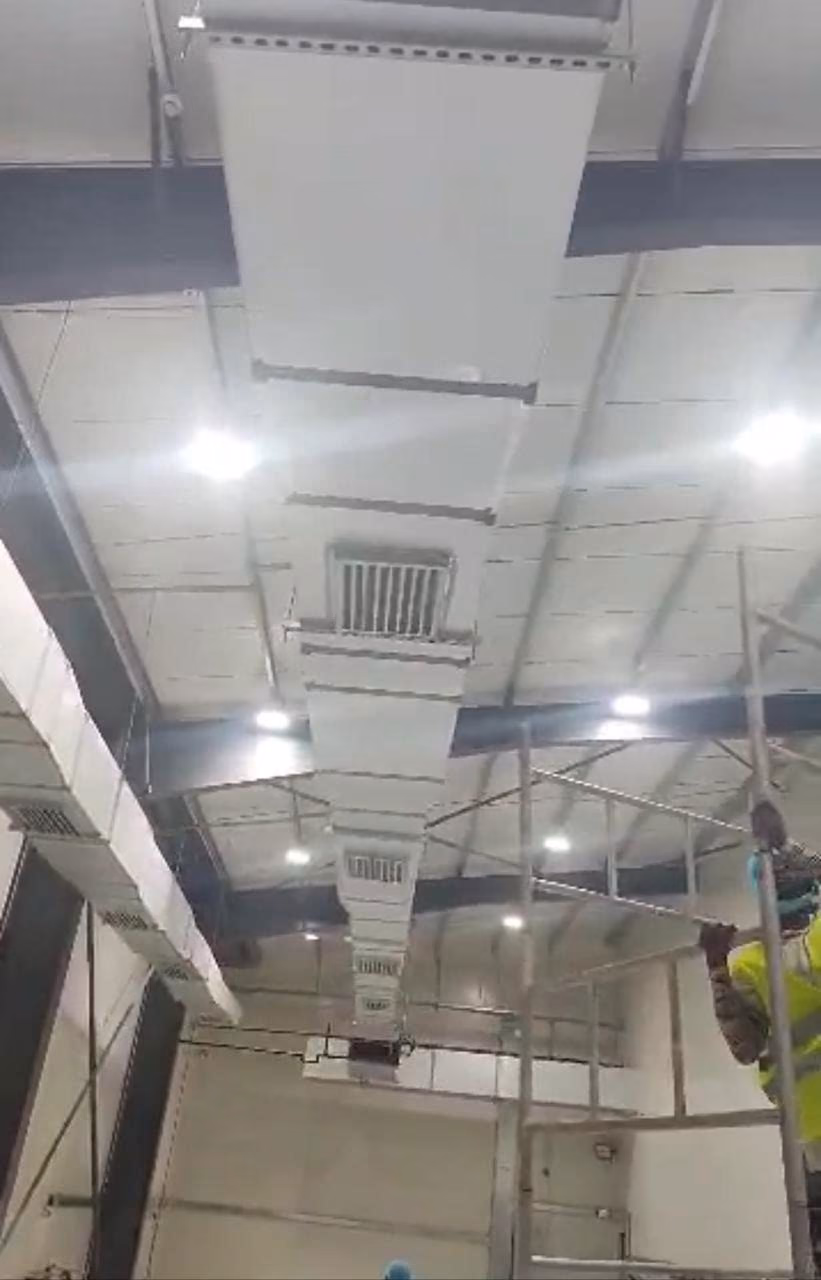 Ductwork and supply grilles under the factory roof, with a PROMEP fitter on a scaffold